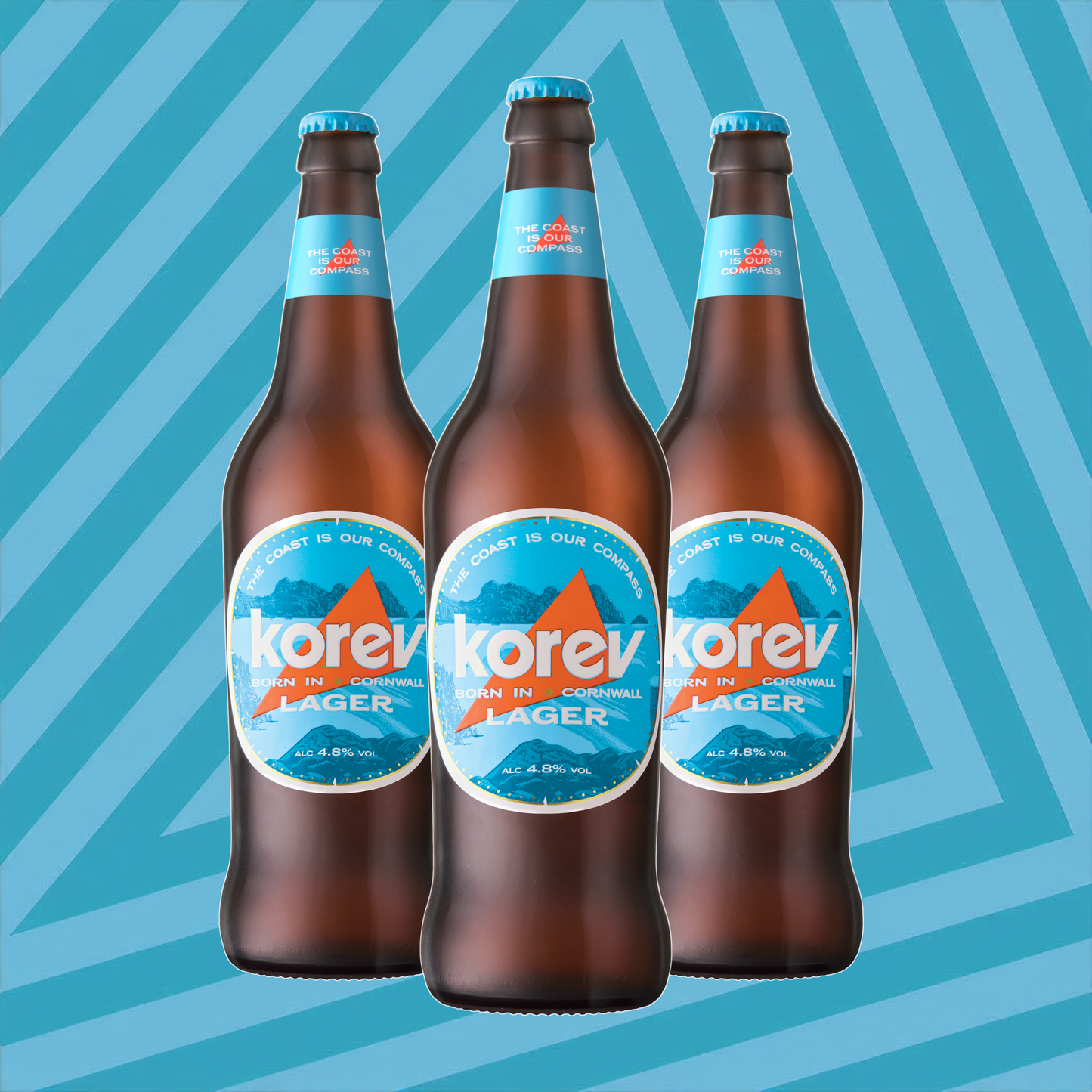 Three brown glass bottles of Korev Lager beer with blue and white labels, arranged in a row against a blue and light blue diagonal striped background.